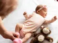 Małe dziecko urodzone w Holandii, w różowym body i opasce z kokardką, leży na białej pościeli obok pluszowego misia.