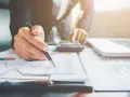Osoba analizuje wykresy i dane, korzystając z kalkulatora i laptopa. Może to być związane z rozliczeniem dodatku zmianowego w Holandii.