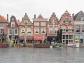Rząd zabytkowych kamienic w Dordrecht, z kawiarnianymi stolikami i parasolami na mokrym bruku. Praca w tym mieście to widok na historię.