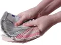 Twee handen tellen een stapel eurobiljetten, waaronder 5 euro biljetten. Een stapel geld, een stipp hollandia.