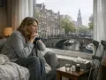 Kobieta z laską patrzy przez okno na Amsterdam. Myśli o swojej przyszłości i o tym, jak sobie poradzi, gdy skończy się renta w Holandii.