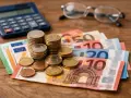 Euro banknoty i monety, kalkulator i okulary. Planowanie emerytury w Holandii wymaga oszczędności.