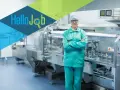 Pracownik w czepku i zielonym uniformie stoi przed linią produkcyjną. Szukasz pracy? Sprawdź cervo oferty pracy!