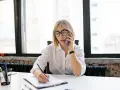 Kobieta w okularach rozmawia przez telefon, notując coś na kartce. Może to dotyczyć sprawy z Belastingdienst i przedawnienia.