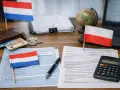 Flagi Holandii i Polski, pieniądze, dokumenty i kalkulator na biurku. Rozliczenie podatkowe, pit zerowy.