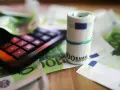 Kalkulator i zwinięte banknoty euro na tle dokumentów. Pomoc w zrozumieniu, jak wypełnić zaświadczenie o dochodach Holandia.