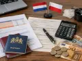 Dokumenty, paszporty, flagi Polski i Holandii, kalkulator i pieniądze sugerują wypłatę składek emerytalnych z Holandii.