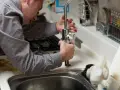 Mężczyzna w paski naprawia kran w kuchni. Fachowiec, hydraulik z Holandii, dba o sprawność instalacji.