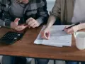 Para rozlicza PIT. Na stole kalkulator, telefon i dokumenty.