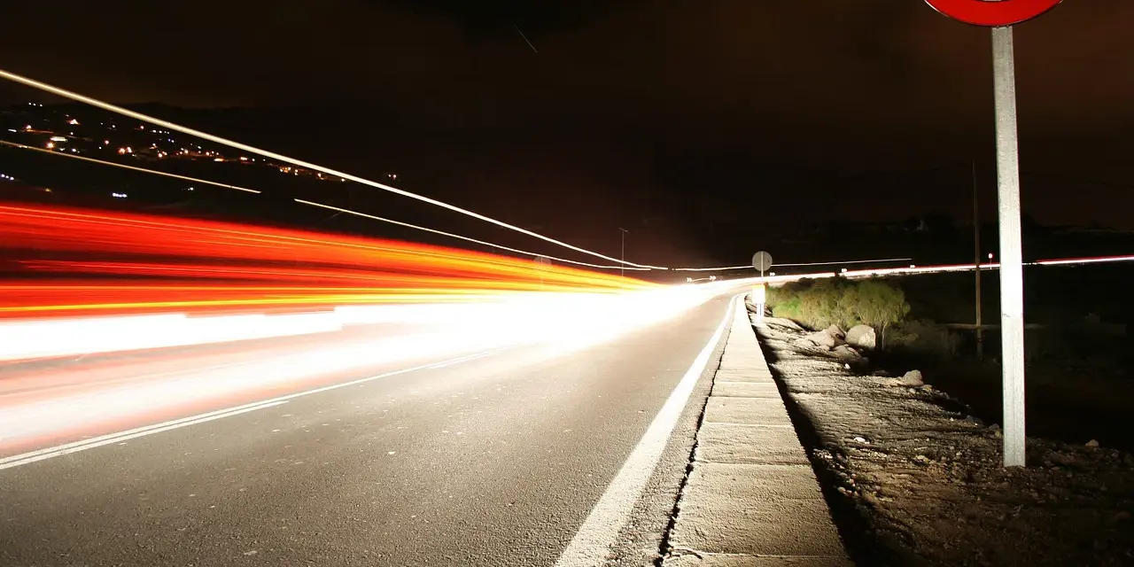 Nocna droga z długimi smugami świateł samochodowych. Znak ograniczenia prędkości 100 km/h przypomina o przepisach, jak ograniczenia prędkości w Holandii.