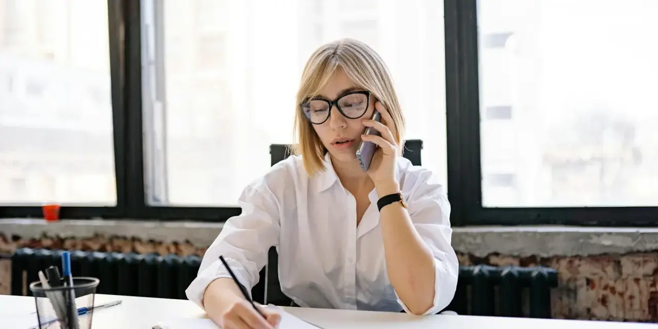 Kobieta w okularach rozmawia przez telefon, notując coś na kartce. Może to dotyczyć sprawy z Belastingdienst i przedawnienia.