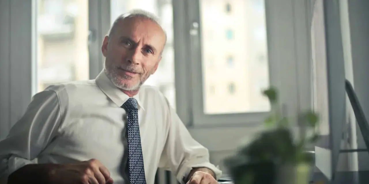 Starszy mężczyzna w białej koszuli i krawacie siedzi przy biurku. Zastanawia się, jak sprawdzić składki emerytalne w Holandii.