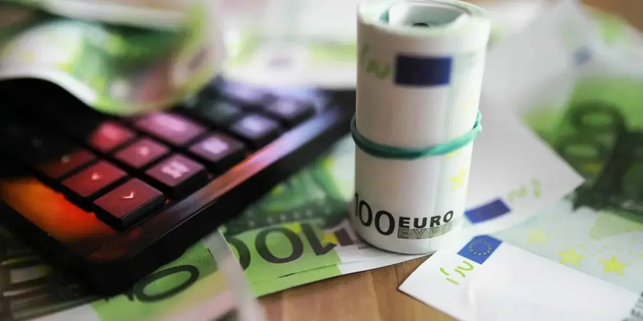 Kalkulator i zwinięte banknoty euro na tle dokumentów. Pomoc w zrozumieniu, jak wypełnić zaświadczenie o dochodach Holandia.