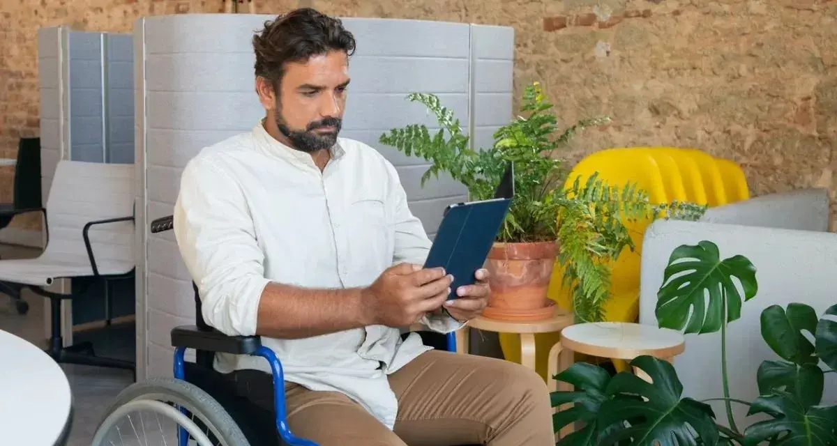 Mężczyzna na wózku inwalidzkim przegląda tablet, szukając informacji o rencie chorobowej w Holandii.