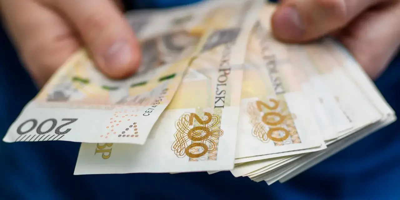 Dłonie trzymają stos banknotów 200 zł. Zastanawiasz się, ile wynosi zasiłek dla bezrobotnych?