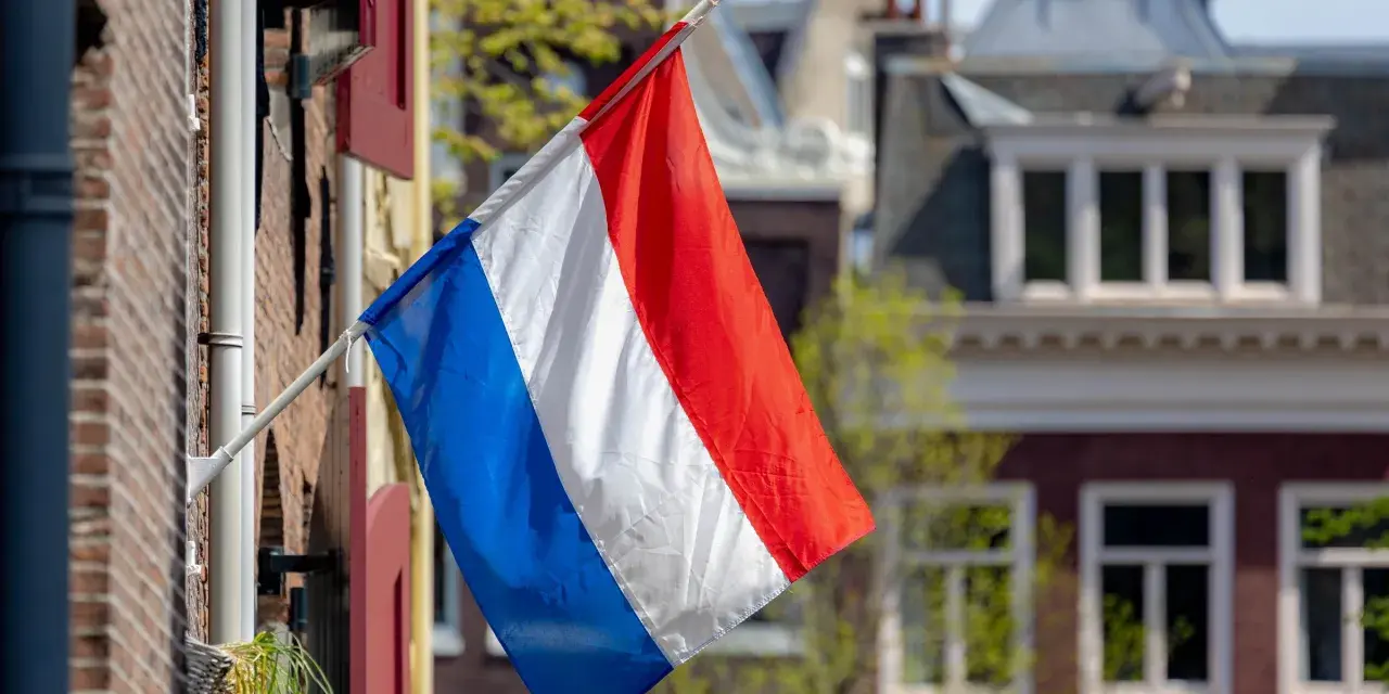 Holenderska flaga powiewa przed domami, które mogą wpływać na ceny domów w Holandii.