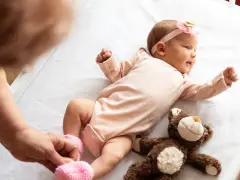 Małe dziecko urodzone w Holandii, w różowym body i opasce z kokardką, leży na białej pościeli obok pluszowego misia.