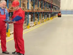 Dwóch pracowników magazynu w Holandii omawia zamówienie. W tle widać regały z towarami i autonomiczne wózki widłowe.
