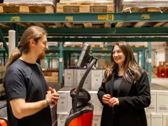 Pracownicy easywork uitzendbureau rozmawiają w magazynie, otoczeni paletami z produktami.