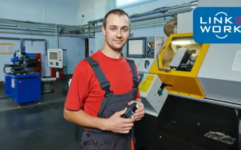 Pracownik w warsztacie w Rotterdamie, gotowy do pracy przy maszynie CNC. Logo Link2Work.