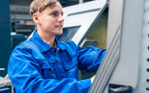 Młody pracownik w niebieskim kombinezonie obsługuje maszynę CNC w Holandii.