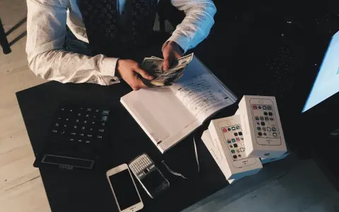 Zliczanie pieniędzy na biurku, kalkulator, telefony i pudełka z iPhone'ami. Rozważanie zzp Holandia koszty.