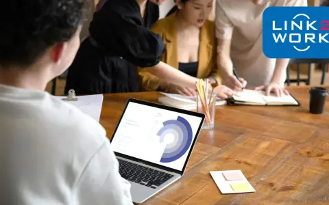 Zespół pracuje nad projektem, analizując dane na laptopie. To idealne miejsce, by zacząć pracę zdalną bez doświadczenia i rozwijać się z Link2Work.
