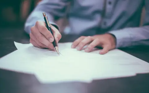 Dłoń pisząca długopisem na dokumencie. Rozważasz otwarcie konta w bankach w Holandii dla Polaków?