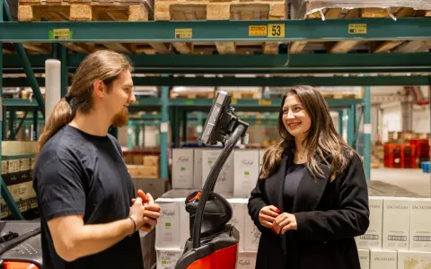 Pracownicy easywork uitzendbureau rozmawiają w magazynie, otoczeni paletami z produktami.