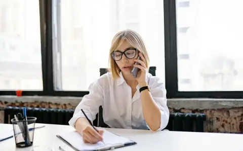Kobieta w okularach rozmawia przez telefon, notując coś na kartce. Może to dotyczyć sprawy z Belastingdienst i przedawnienia.