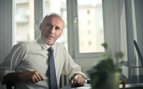 Starszy mężczyzna w białej koszuli i krawacie siedzi przy biurku. Zastanawia się, jak sprawdzić składki emerytalne w Holandii.