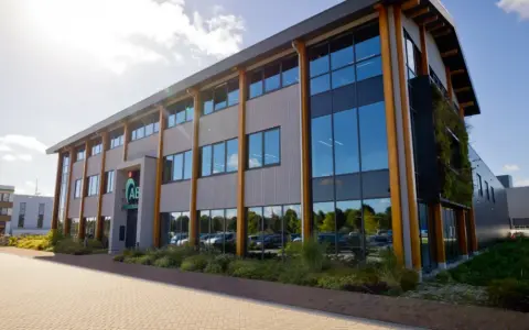 Nowoczesny budynek z drewnianymi elementami, logo AB Midden Nederland.