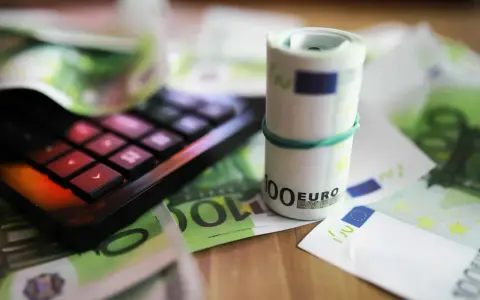 Kalkulator i zwinięte banknoty euro na tle dokumentów. Pomoc w zrozumieniu, jak wypełnić zaświadczenie o dochodach Holandia.