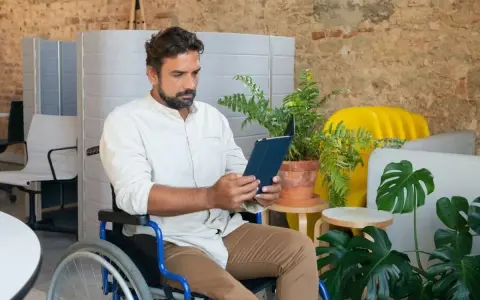 Mężczyzna na wózku inwalidzkim przegląda tablet, szukając informacji o rencie chorobowej w Holandii.
