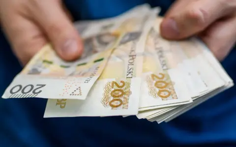 Dłonie trzymają stos banknotów 200 zł. Zastanawiasz się, ile wynosi zasiłek dla bezrobotnych?