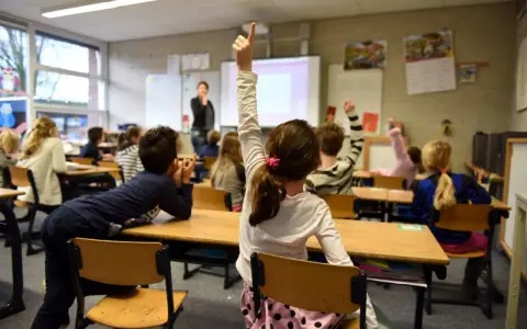Dzieci na lekcji w Holandii, z podniesionymi rękami. Dowiedz się, jak zapisać dziecko do szkoły w Holandii.