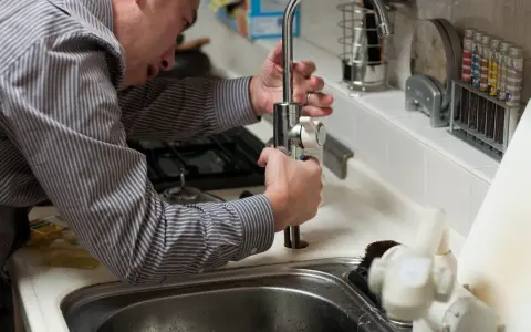 Mężczyzna w paski naprawia kran w kuchni. Fachowiec, hydraulik z Holandii, dba o sprawność instalacji.