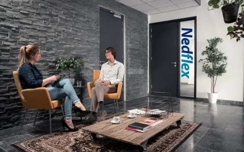 Rozmowa o pracy w Leeuwarden. Kobieta z tabletem i mężczyzna w okularach siedzą w poczekalni firmy Nedflex.