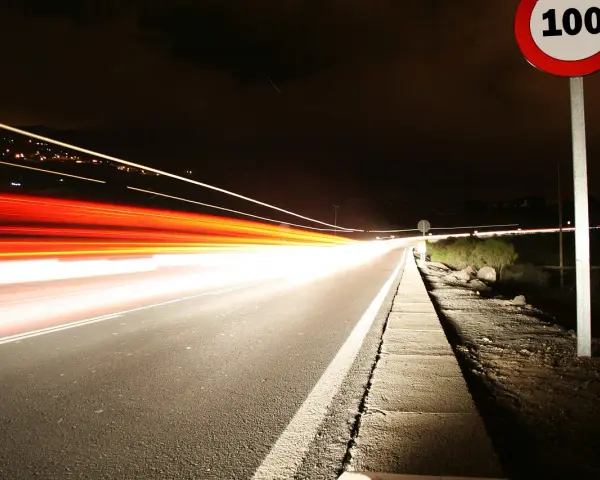 Nocna droga z długimi smugami świateł samochodowych. Znak ograniczenia prędkości 100 km/h przypomina o przepisach, jak ograniczenia prędkości w Holandii.