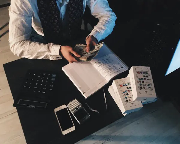 Zliczanie pieniędzy na biurku, kalkulator, telefony i pudełka z iPhone'ami. Rozważanie zzp Holandia koszty.