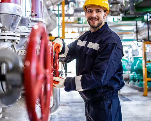 Vrolijke operator koparki holandia, met gele helm, draait aan rode kraan in industriële omgeving.