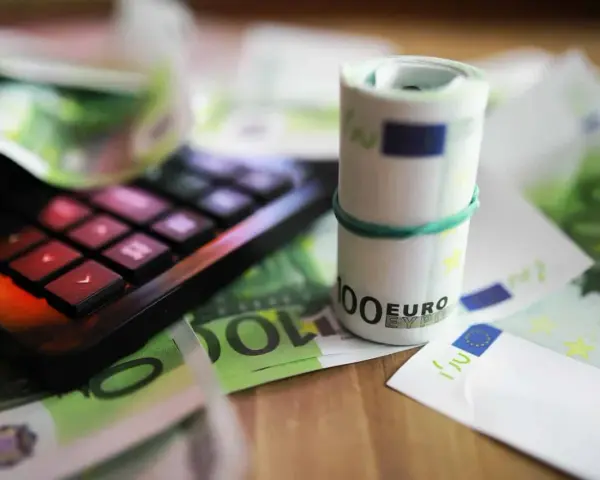 Kalkulator i zwinięte banknoty euro na tle dokumentów. Pomoc w zrozumieniu, jak wypełnić zaświadczenie o dochodach Holandia.