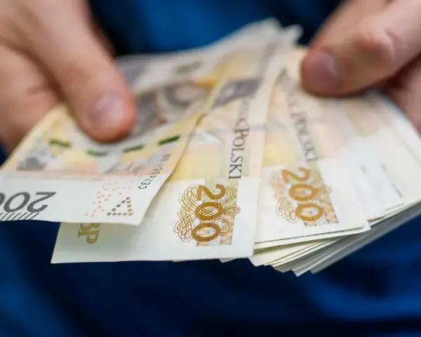 Dłonie trzymają stos banknotów 200 zł. Zastanawiasz się, ile wynosi zasiłek dla bezrobotnych?