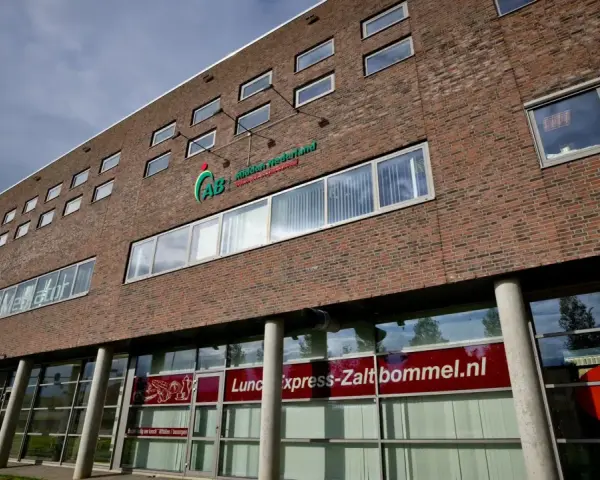 Nowoczesny budynek z cegły z logo AB Midden Nederland. Na parterze szyld "Lunch express-Zaltbommel.nl".