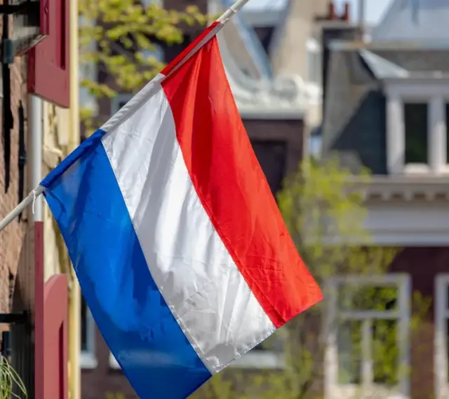 Holenderska flaga powiewa przed domami, które mogą wpływać na ceny domów w Holandii.