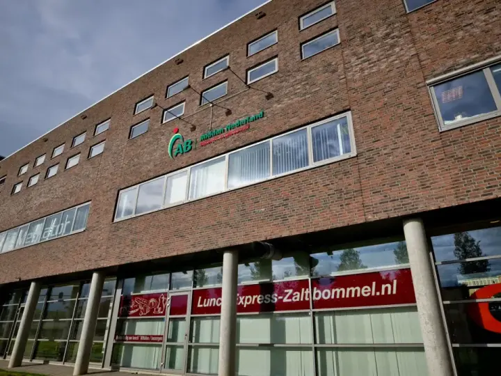 Nowoczesny budynek z cegły z logo AB Midden Nederland. Na parterze szyld "Lunch express-Zaltbommel.nl".