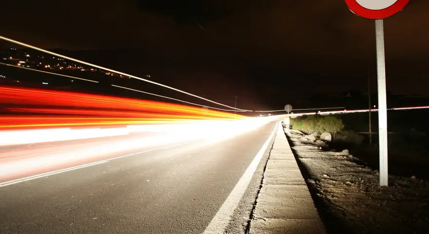Nocna droga z długimi smugami świateł samochodowych. Znak ograniczenia prędkości 100 km/h przypomina o przepisach, jak ograniczenia prędkości w Holandii.