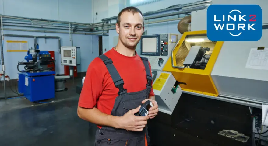 Pracownik w warsztacie w Rotterdamie, gotowy do pracy przy maszynie CNC. Logo Link2Work.