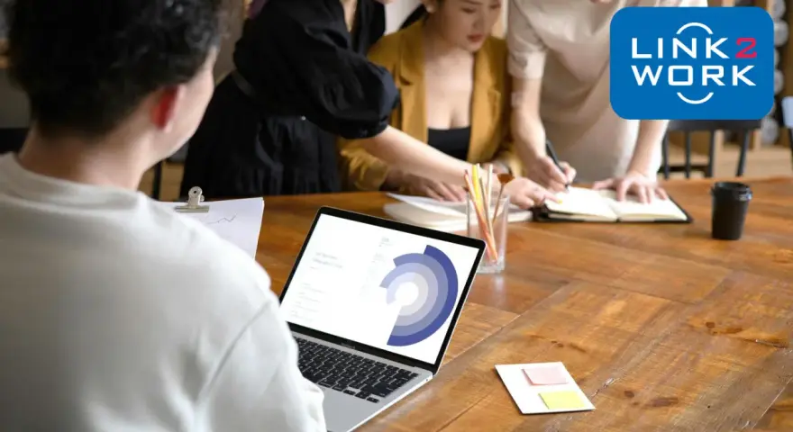 Zespół pracuje nad projektem, analizując dane na laptopie. To idealne miejsce, by zacząć pracę zdalną bez doświadczenia i rozwijać się z Link2Work.