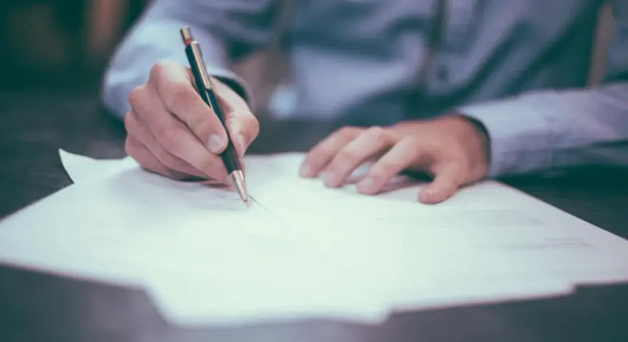Dłoń pisząca długopisem na dokumencie. Rozważasz otwarcie konta w bankach w Holandii dla Polaków?